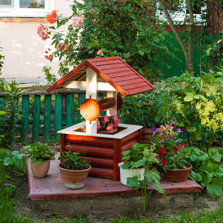 Stock photo of a small garden in the backyard. Fake well with potted flowers. Rustic backyard in countryside or village.